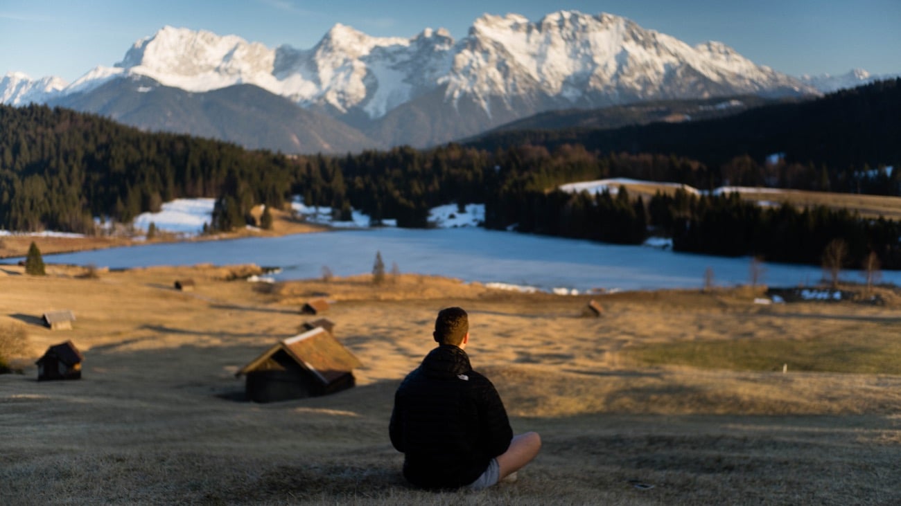 man siting cross legged in front of a mountain practising yoga