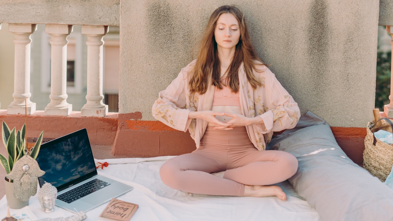 woman practising yoga outside with a laptop beside her